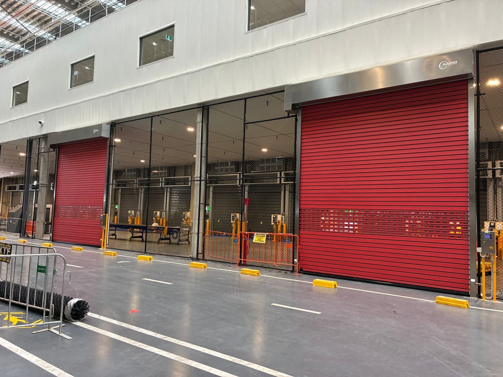Two red high-speed doors installed along a warehouse production aisle.