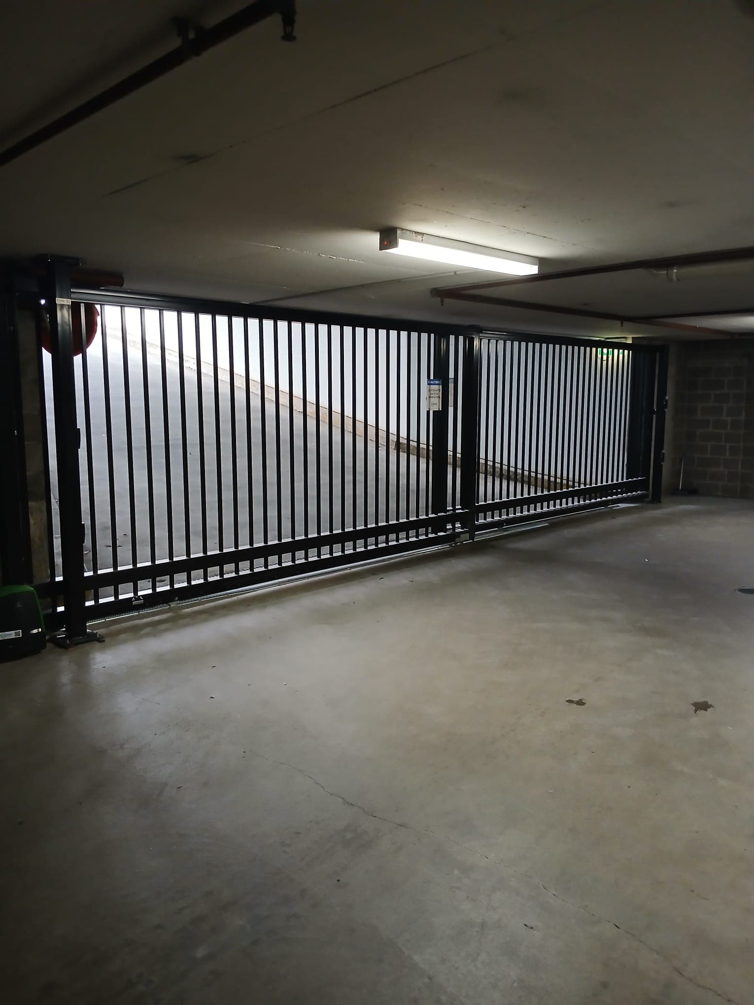 Closed black telescopic gate spanning an indoor car park entrance.