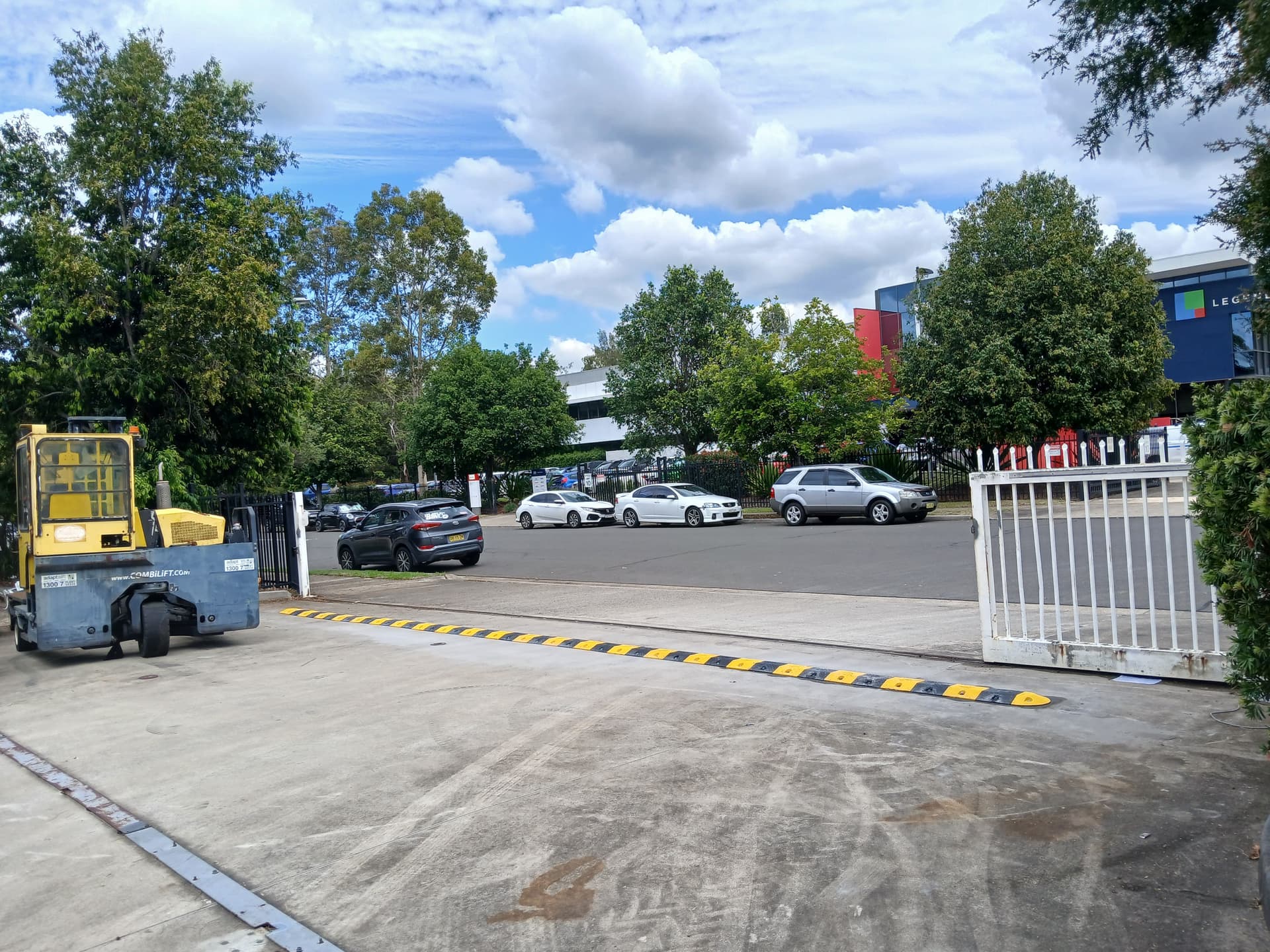 White commercial sliding gate beside a speed hump and busy car park