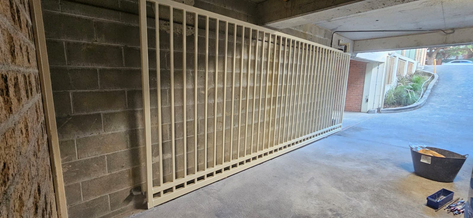 Cream sliding gate running closely along a concrete car-park wall