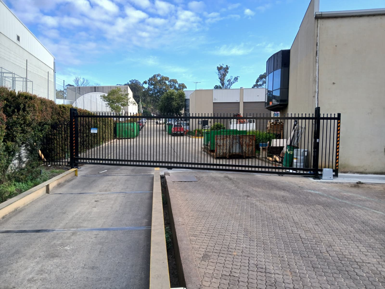 Black sliding gate closed across a commercial driveway with safety-marked posts.