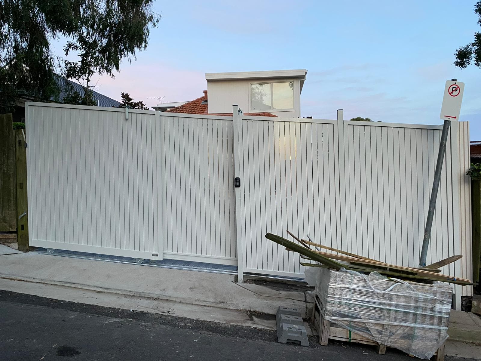 White residential sliding gate frontage with a pedestrian gate and driveway.
