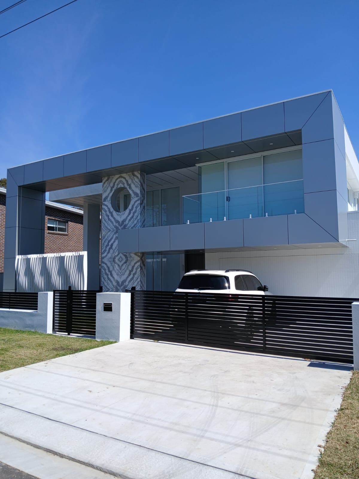 Black horizontal-slat sliding gate across the driveway of a modern two-storey home