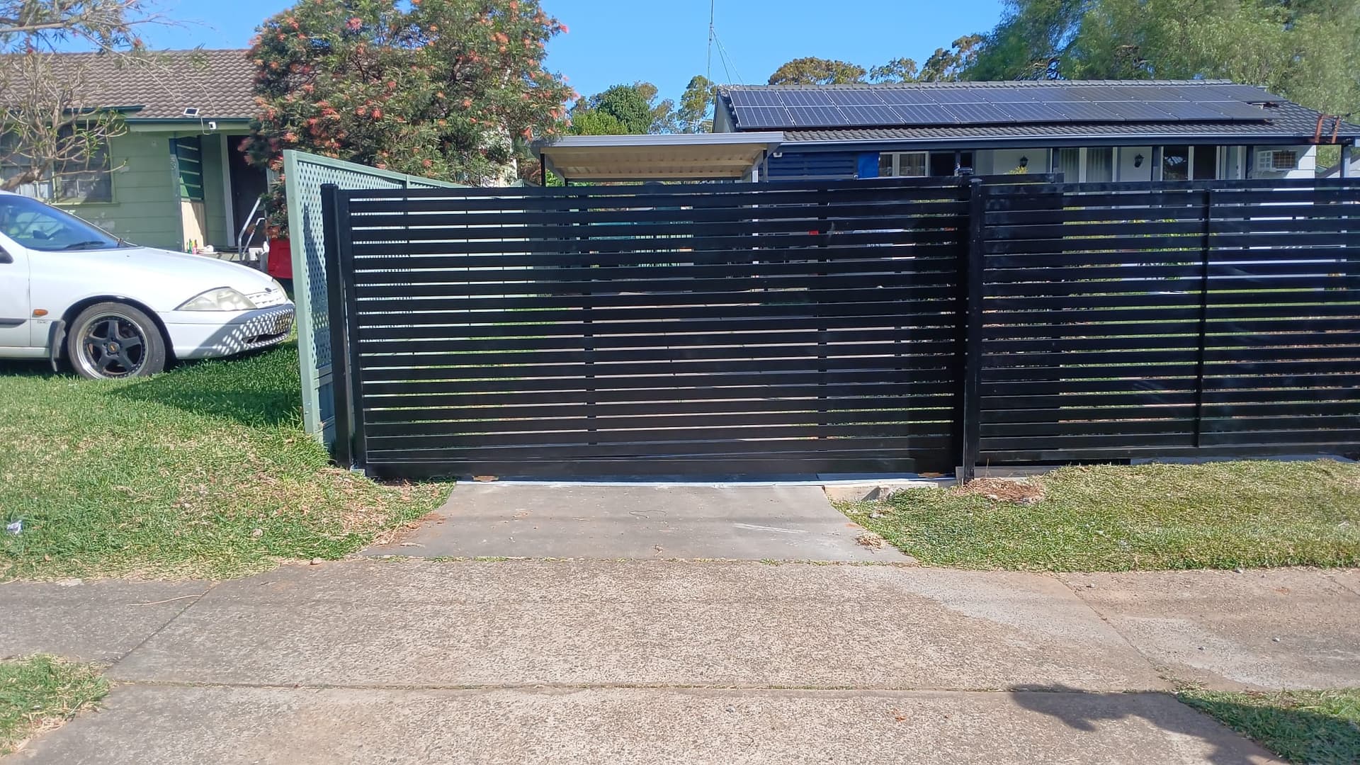 Black horizontal-slat sliding gate across a residential driveway