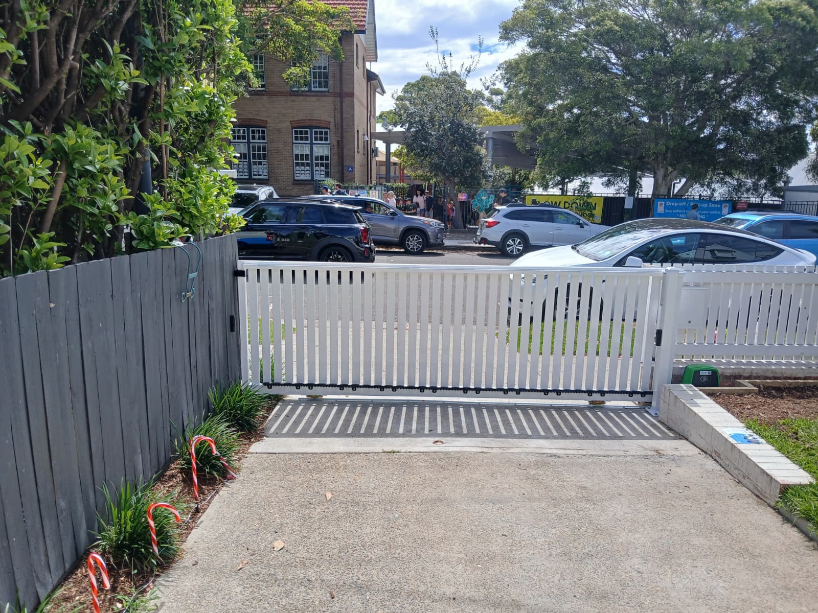 White sliding gate across a residential driveway that slopes down toward the street