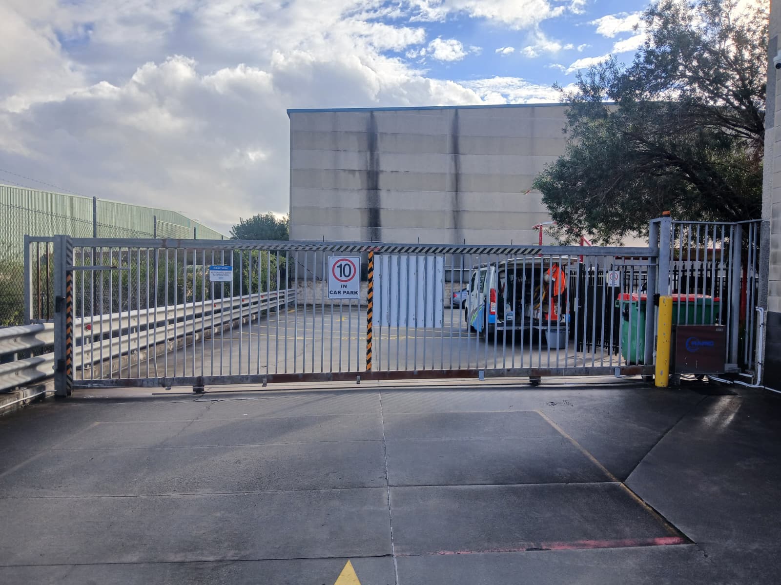 Automatic sliding security gate with speed signage, safety markings and a gate operator at a commercial facility
