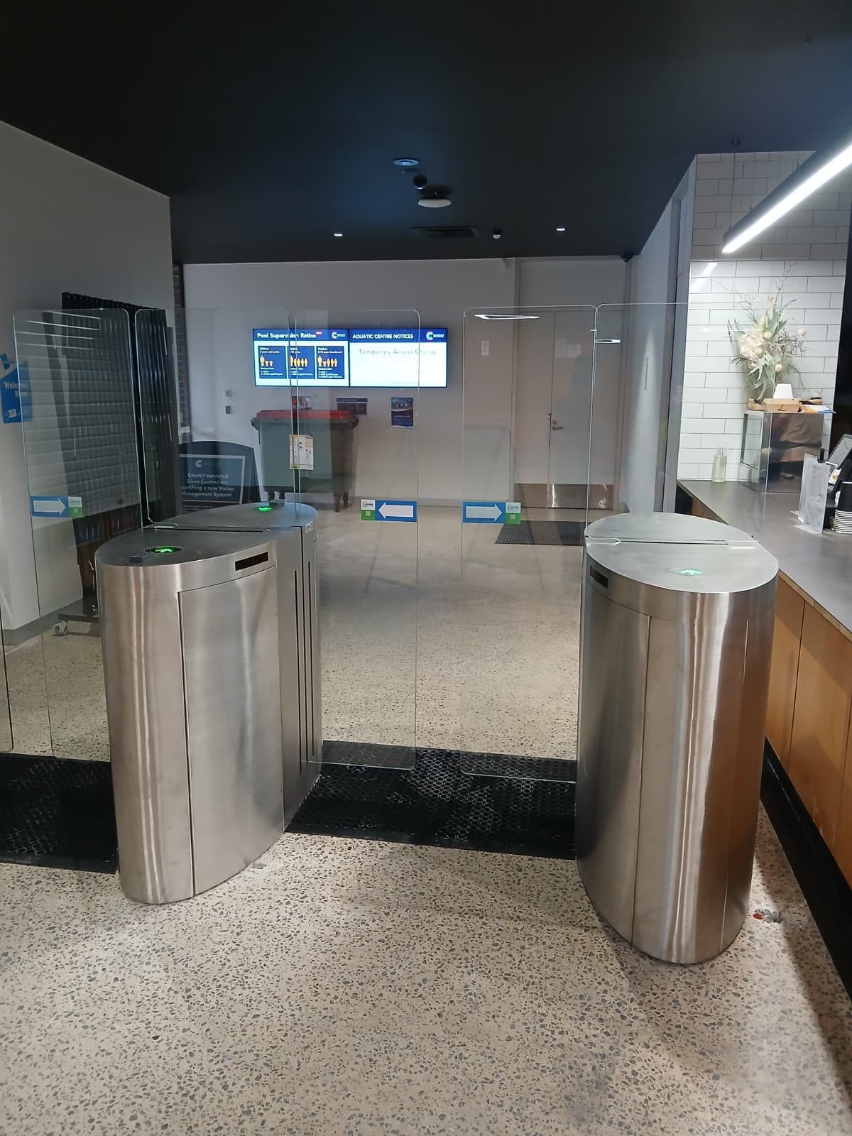 Two stainless speed gates with glass wings in a finished commercial lobby.