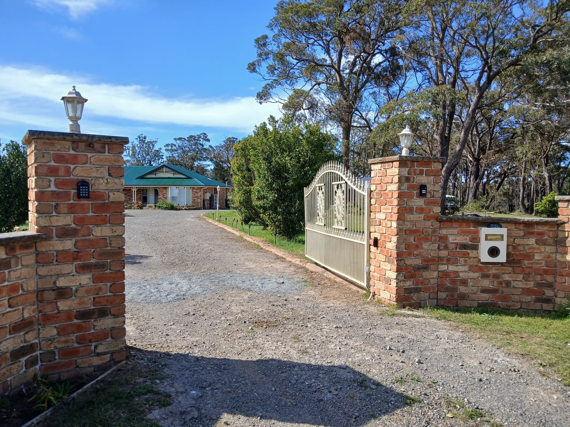 Wide cream ornamental gates between brick pillars at a landscaped entrance
