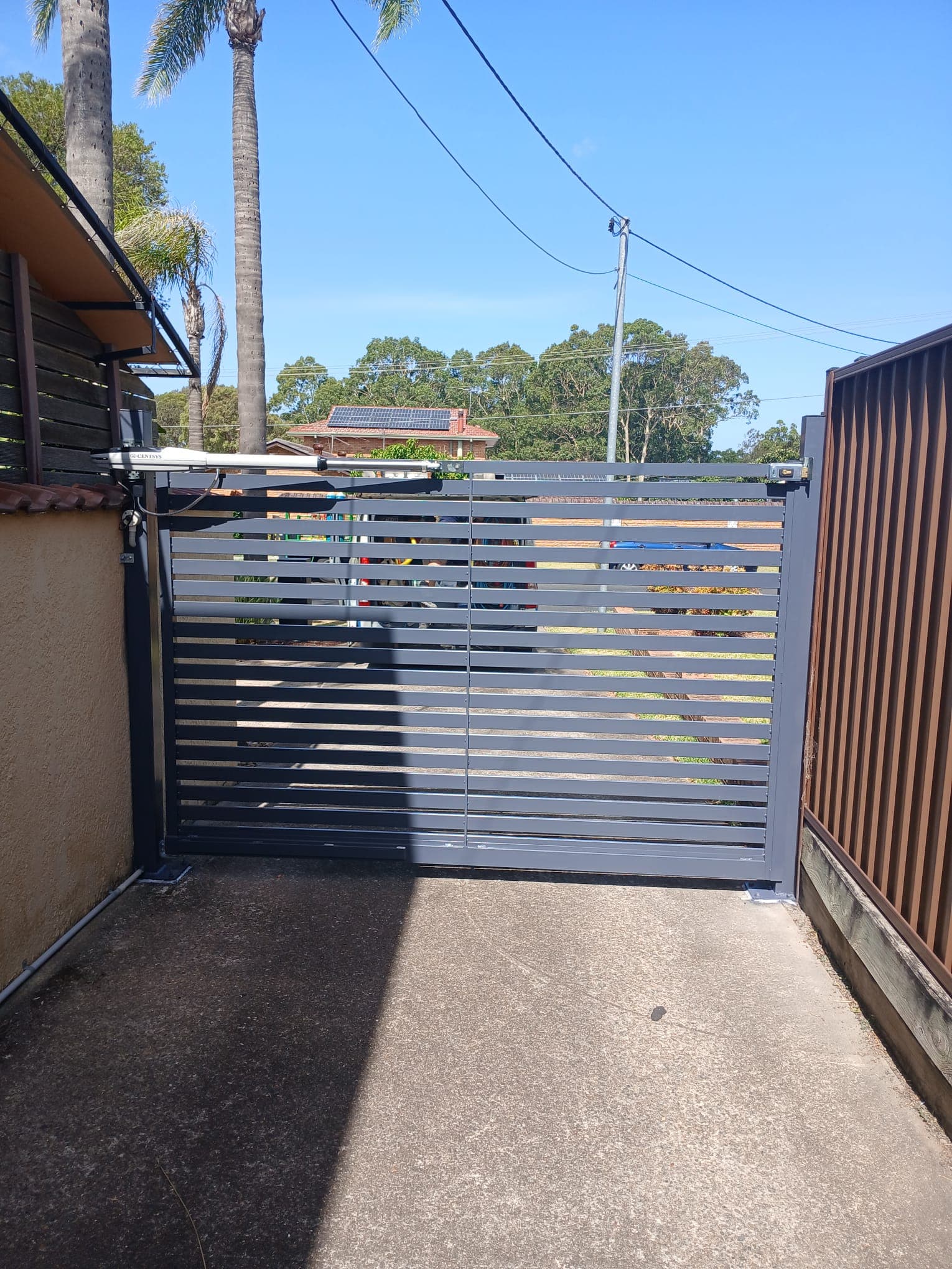 Closed grey double swing gates across a narrow residential driveway