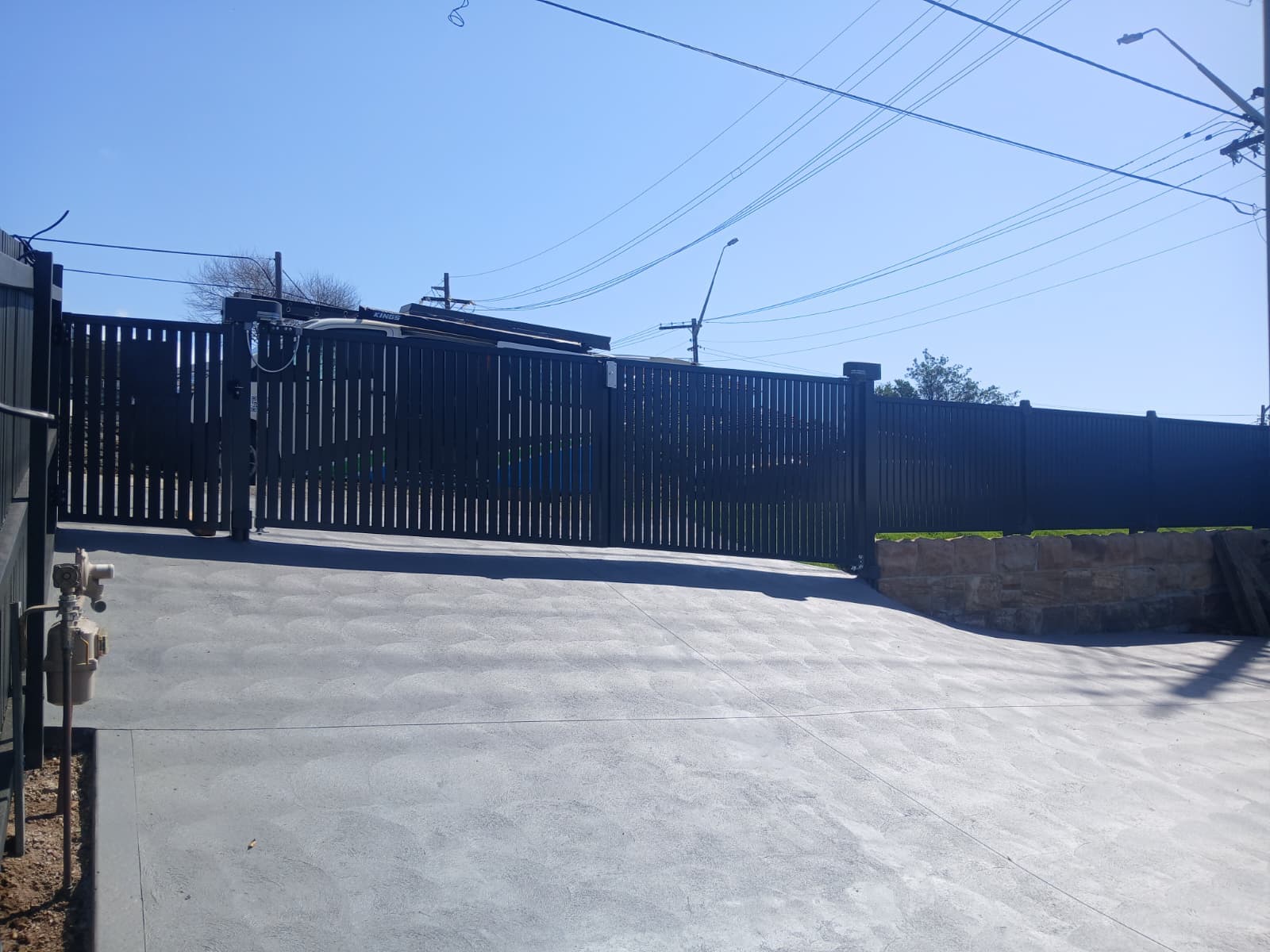 Closed black double swing gates across a broad residential driveway