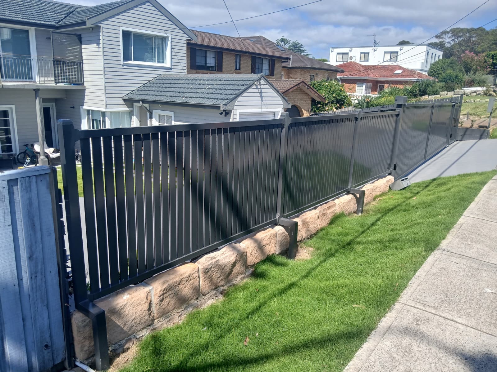 Black swing gate integrated into a boundary fence beside a public footpath