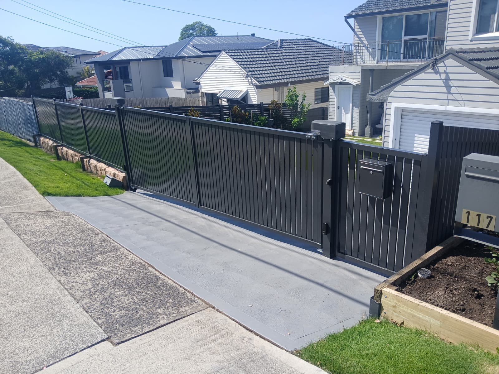 Black swing gate across a sloping residential driveway