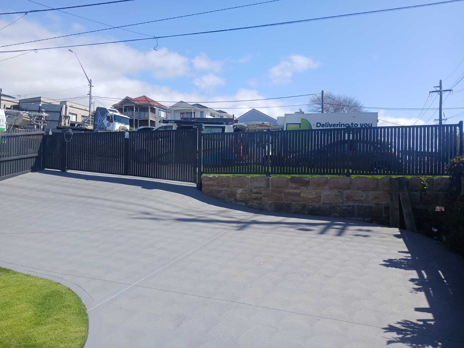 Black swing gates beside a sandstone retaining wall and curved driveway