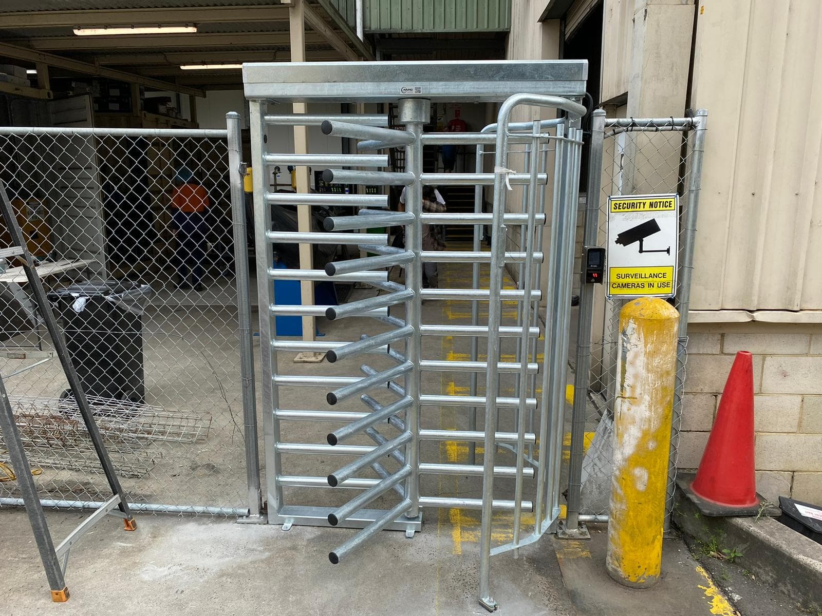 Full-height turnstile with access reader and surveillance signage at an industrial entrance