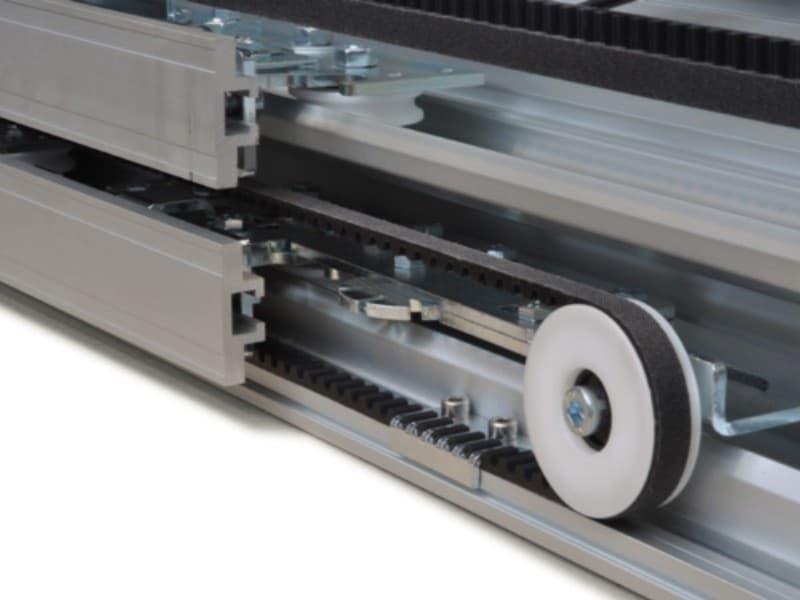 Close-up of an automatic sliding door track system showing dual rollers, belt-driven mechanism, and aluminium guide rails for smooth and precise door movement.