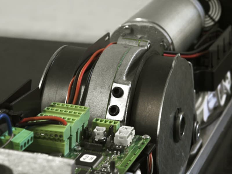 Close-up of the motor and control circuitry inside an automatic swing door operator, showing gear mechanism, wiring, and terminal connectors for system integration.