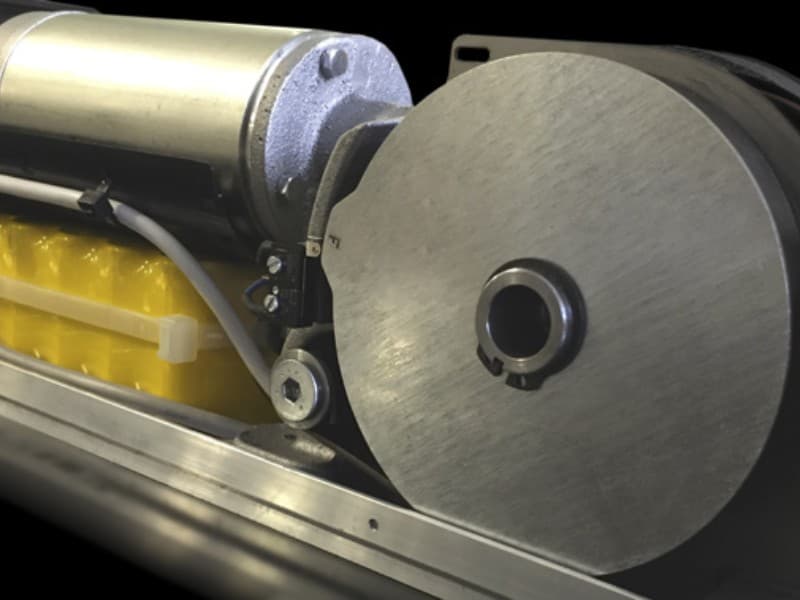 Detailed view of the motor and gear assembly in an automatic swing door operator, featuring a cylindrical drive unit, yellow battery pack, and metal pulley system.