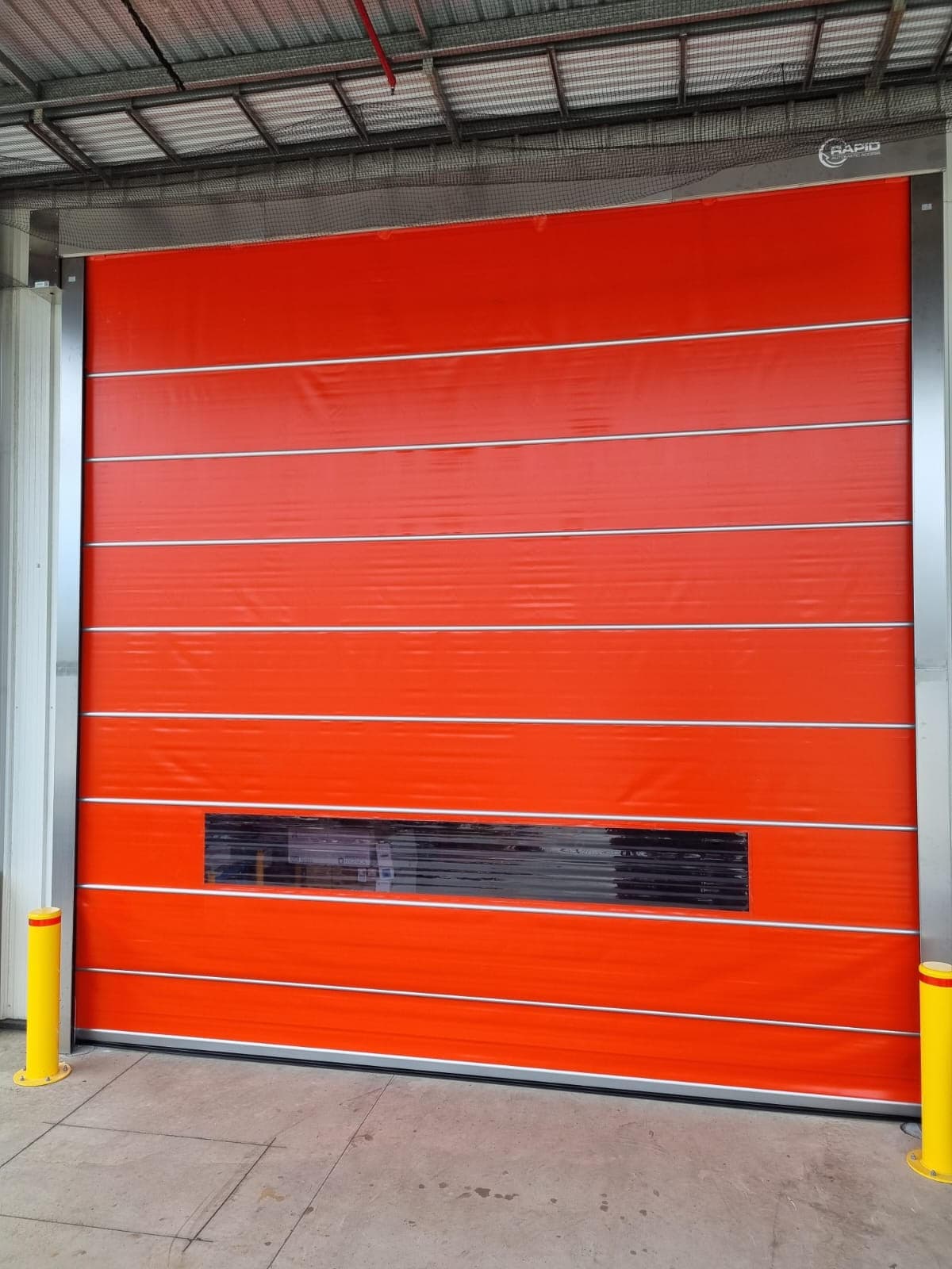 Warehouse high-speed door with safety bollards, shot from outside.