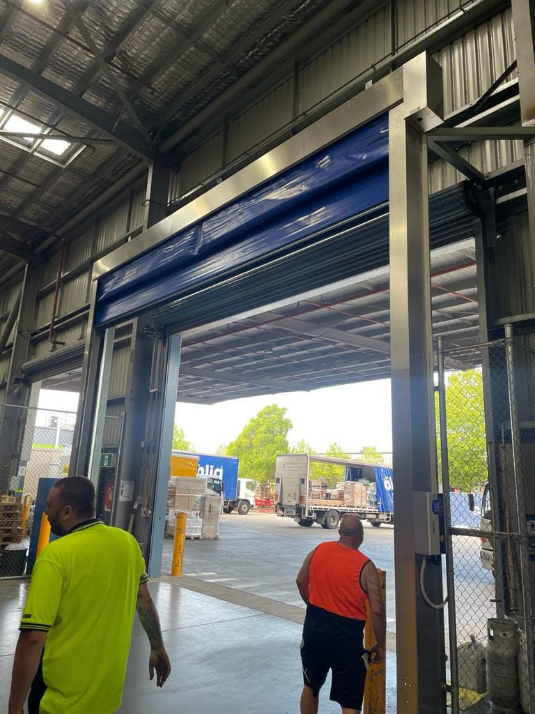 Large warehouse high-speed door at customs depot, open with workers standing nearby.