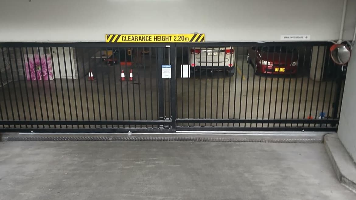 Automatic sliding gate at basement parking entry with clearance height signage.