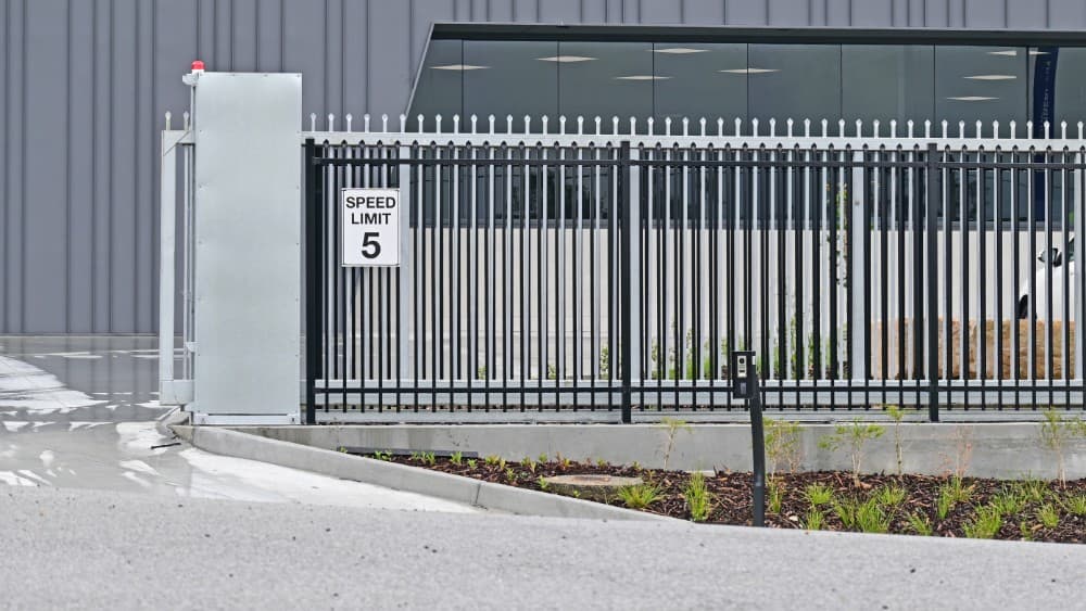 Sliding security gate at a factory driveway with speed limit signage.