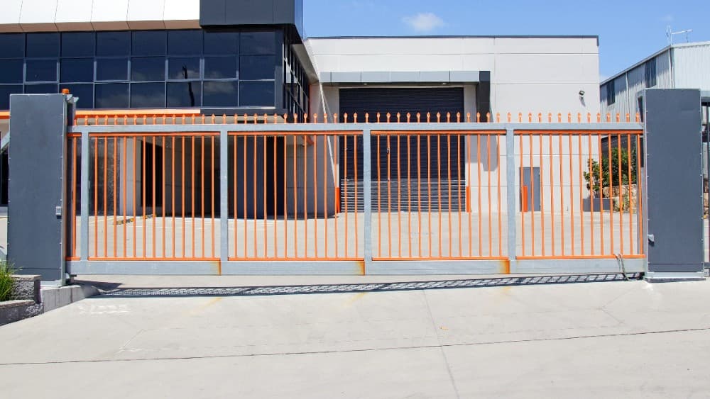 Security sliding gate with orange accents at a warehouse entrance.