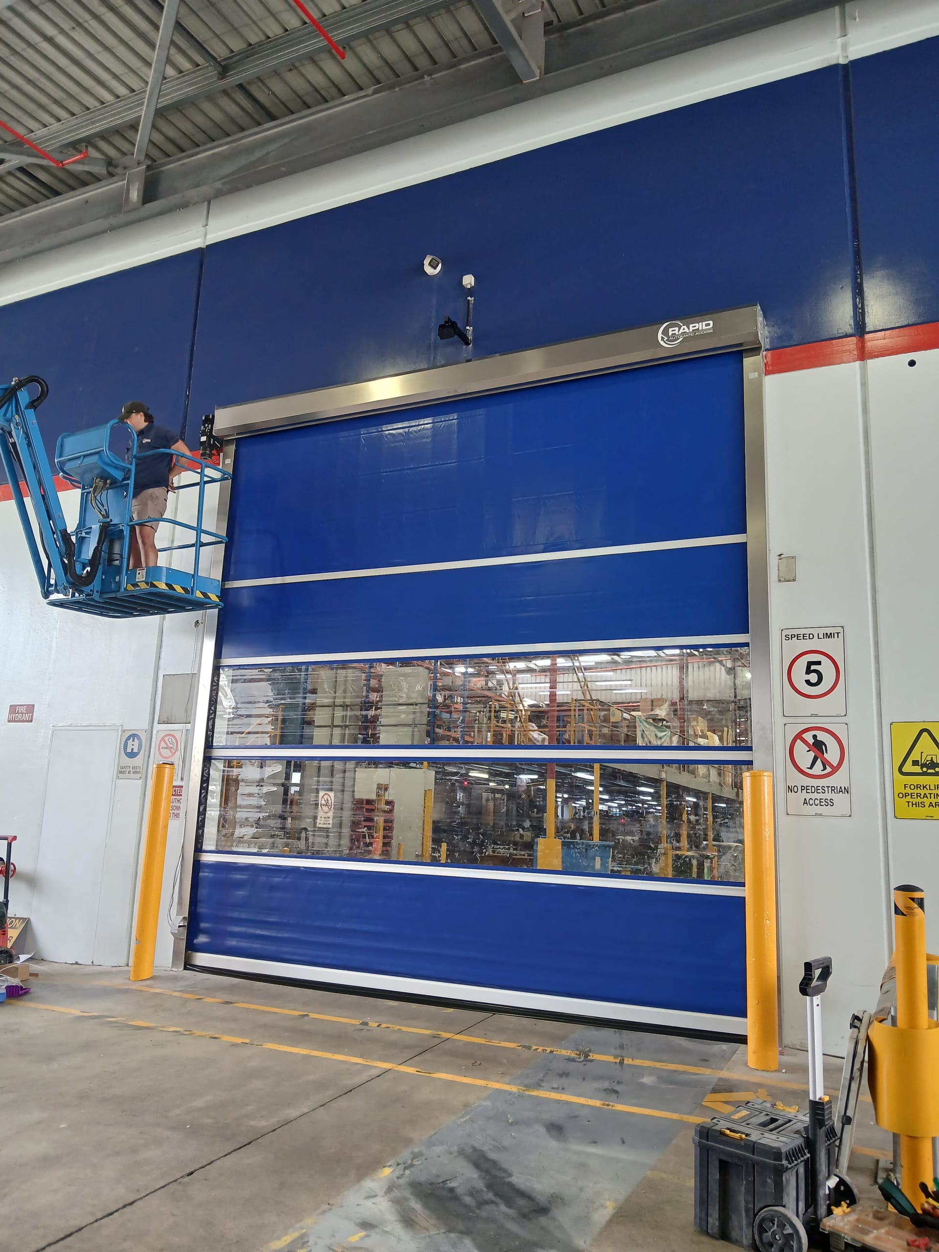 Rapid technician servicing a blue high-speed warehouse door from a lift.