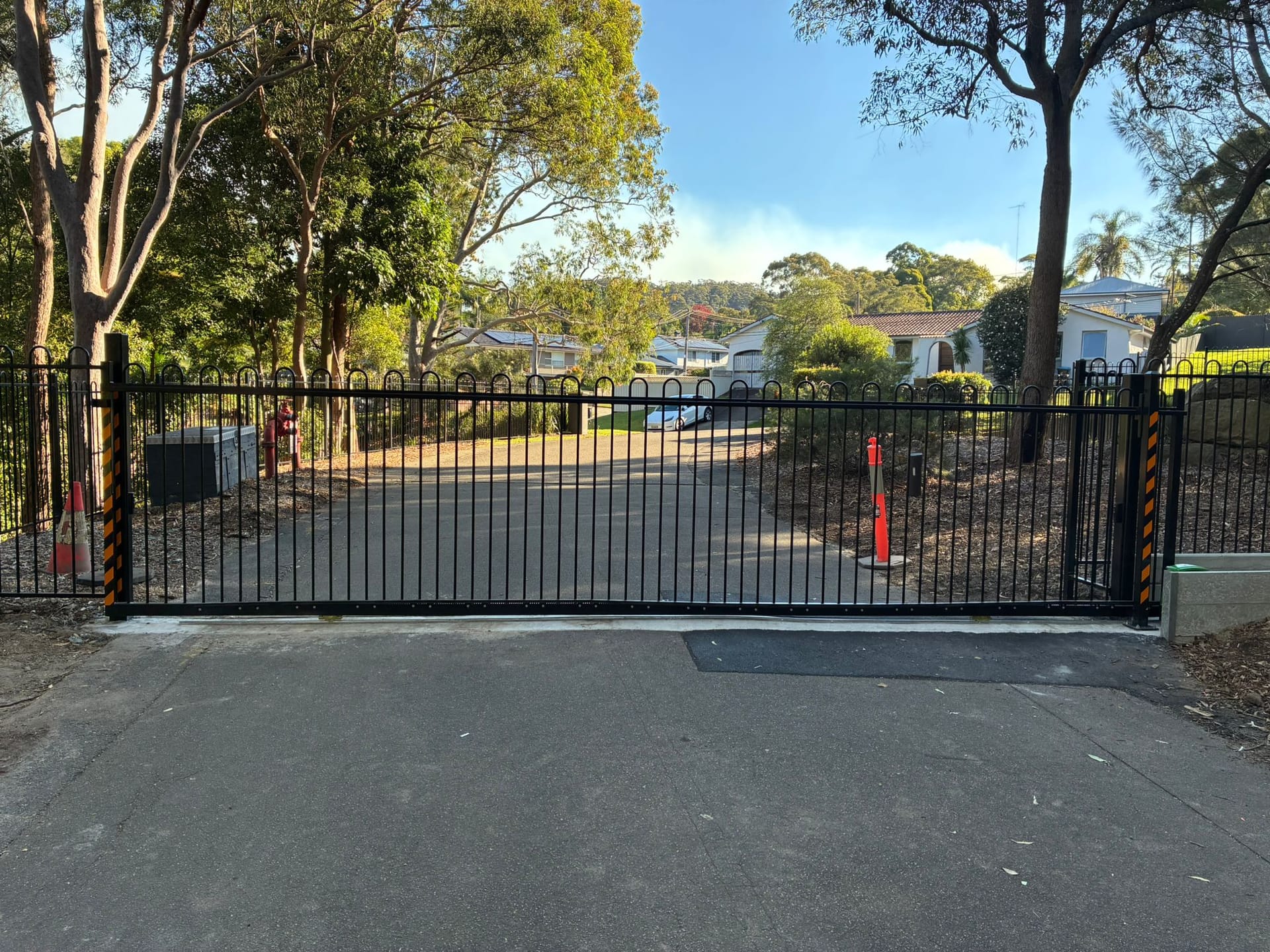 Black sliding gate installed at a tree-lined facility entrance.