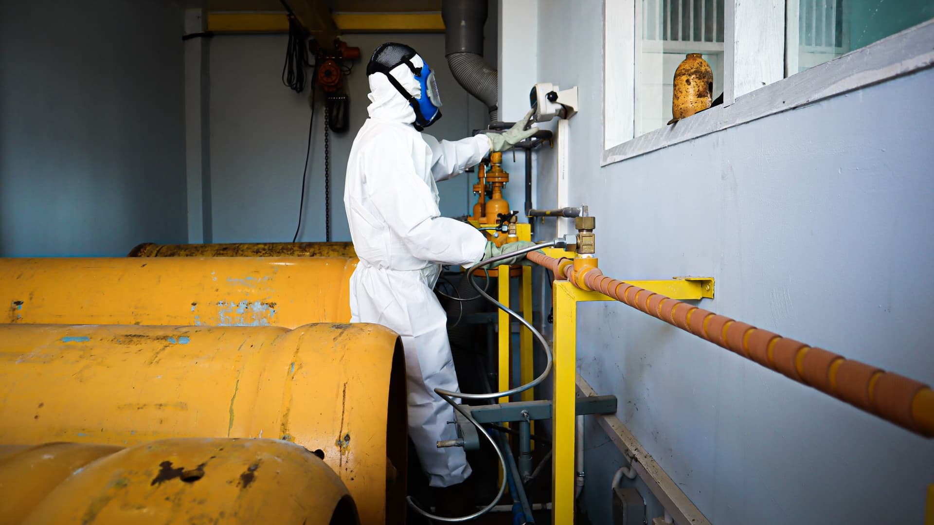 Worker wearing protective clothing and a respirator while operating industrial pipework