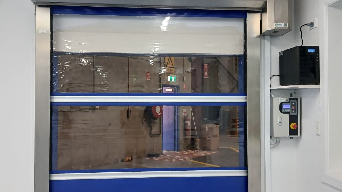 Closed blue high-speed door with stainless frame, controller and air unit inside a contamination-controlled facility