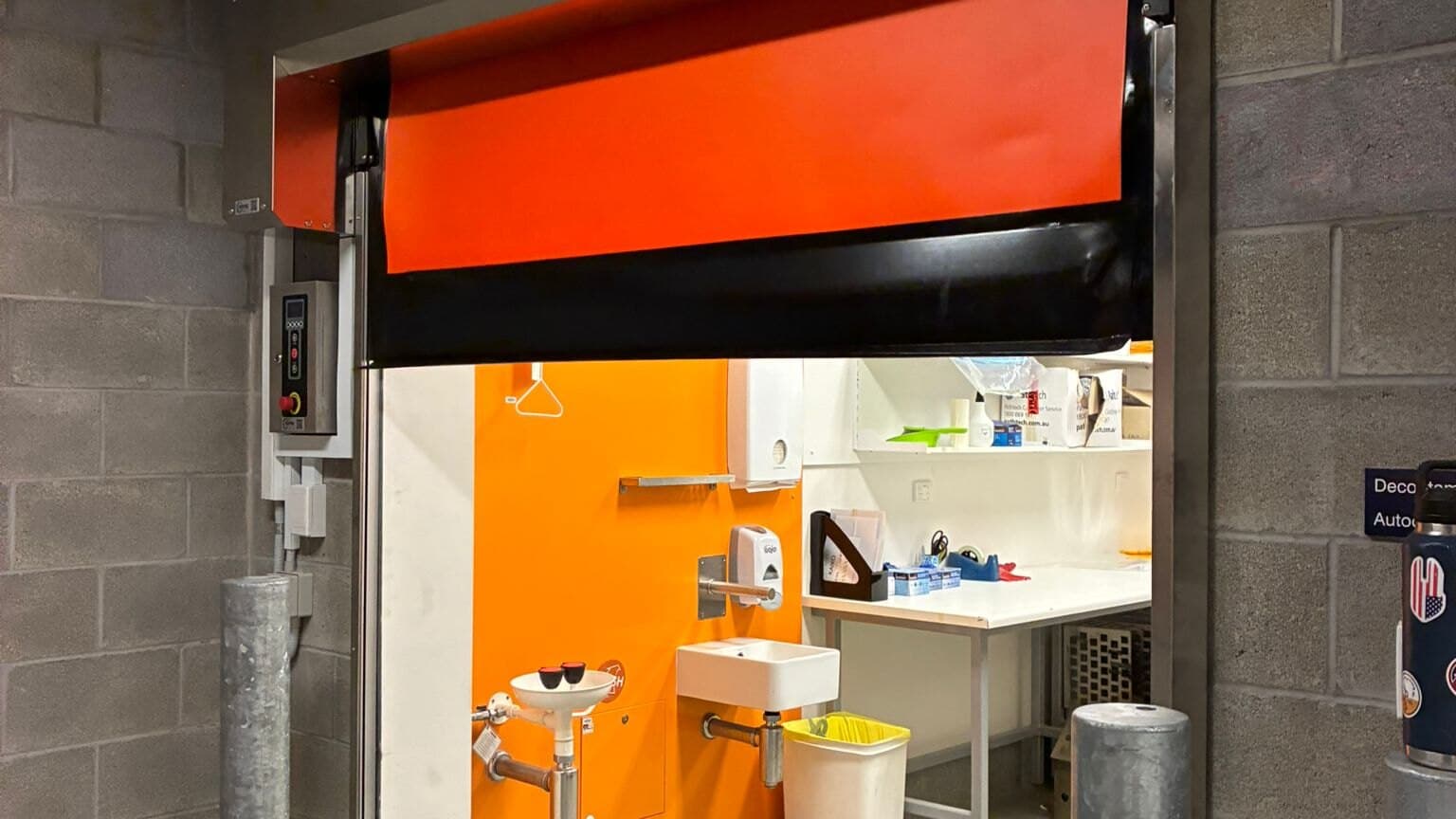 Open red high-speed door separating an industrial passage from a smaller internal workroom