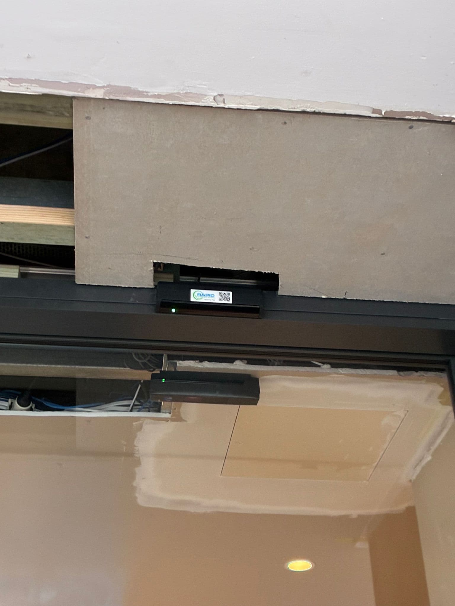 Automatic door sensor mounted on a black storefront header above a glass entrance