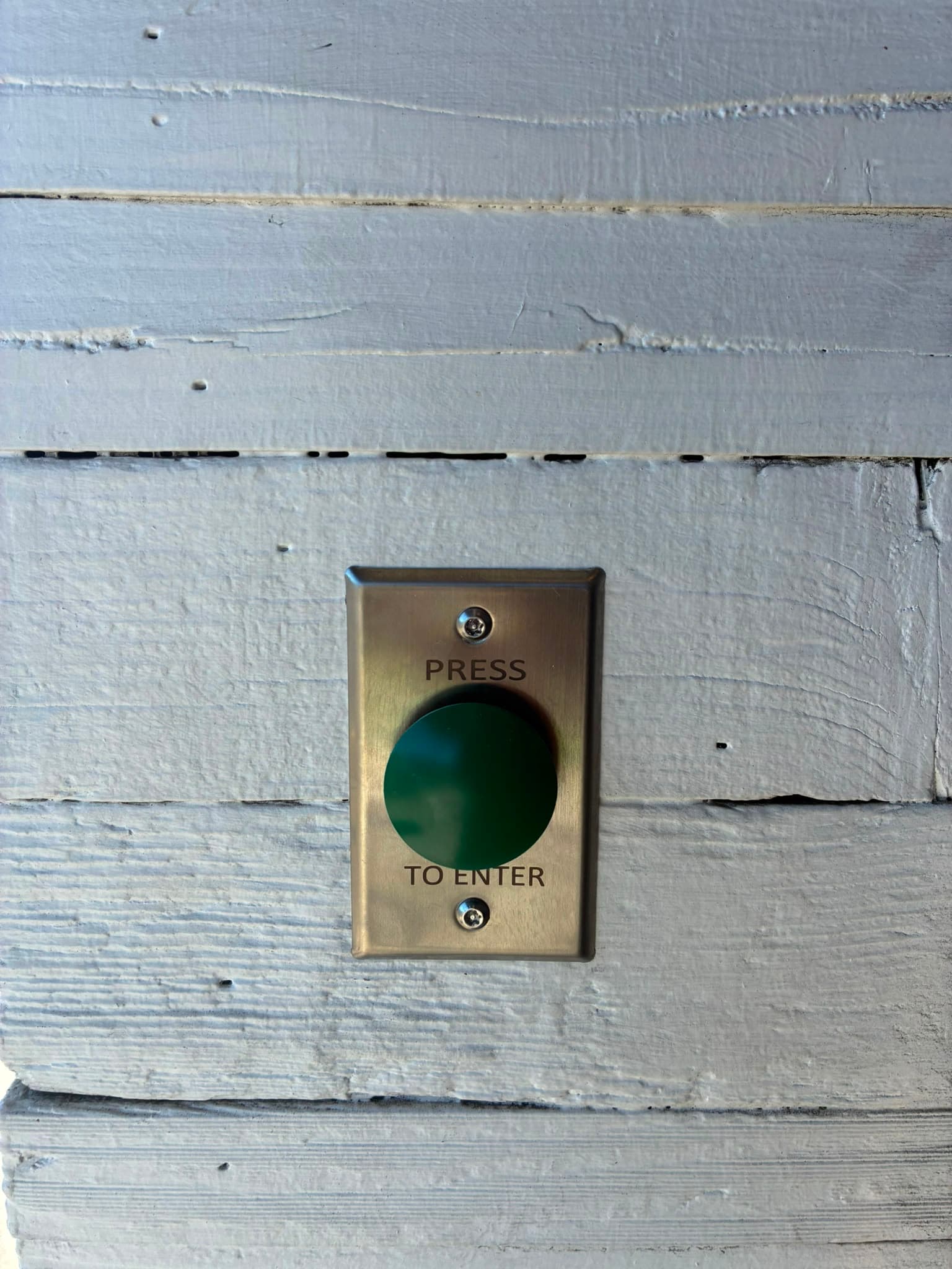 Green press-to-enter button installed beside an automatic retail door