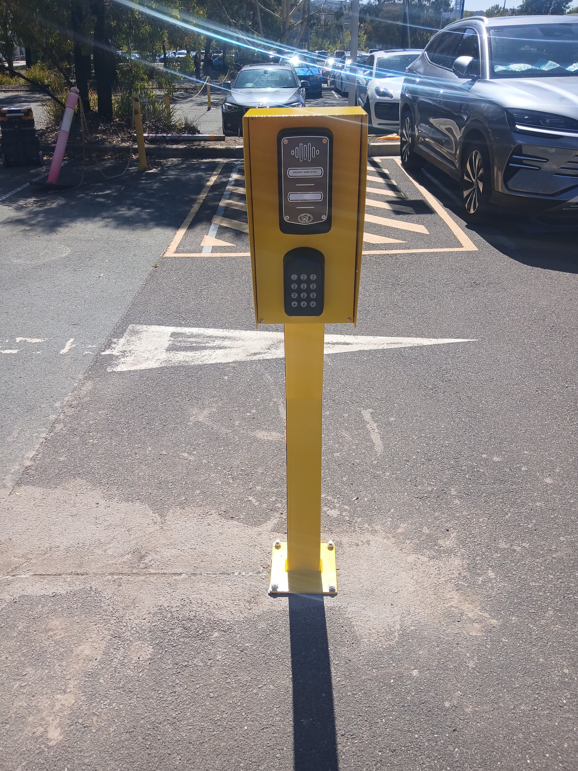 Yellow intercom and keypad pedestal for car park vehicle access control.