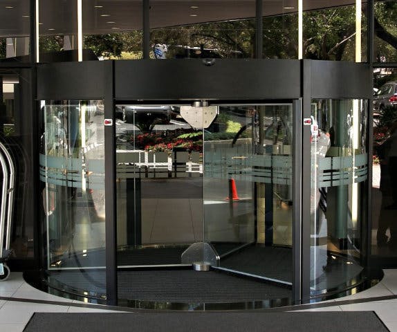 A large black automatic revolving door serving as the entry point to a large retail shopping complex.