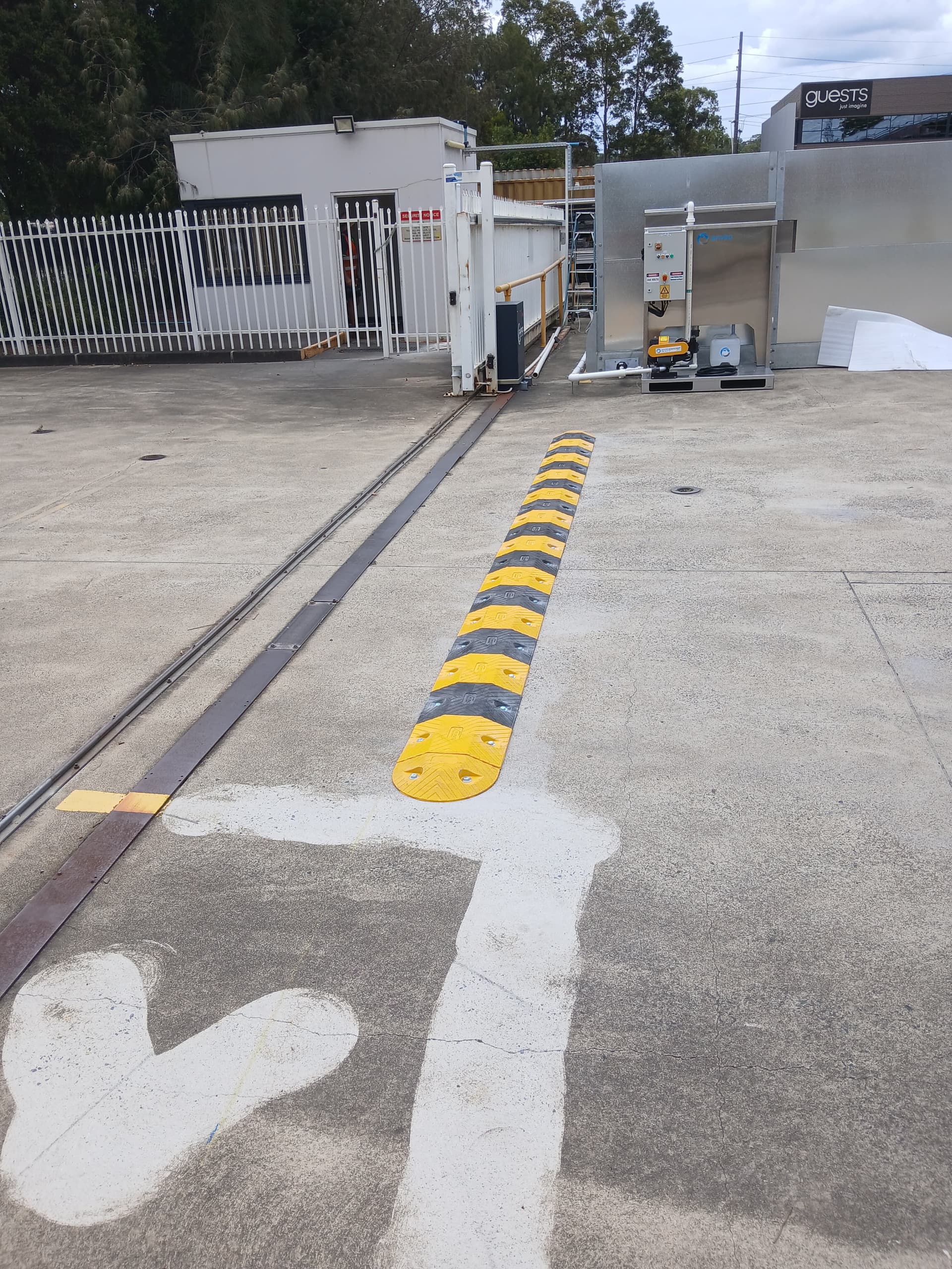 Commercial sliding gate track crossing a driveway beside a speed hump.