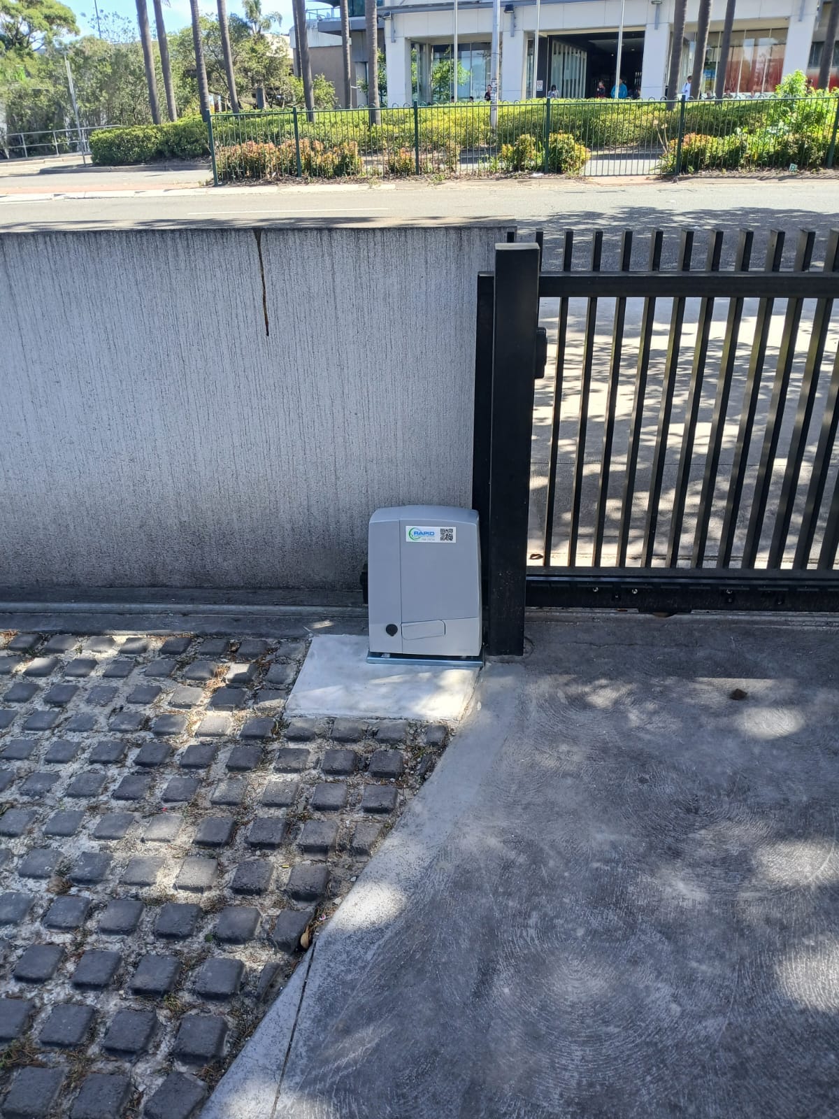 Sliding gate motor installed beside a black metal sliding gate and track.