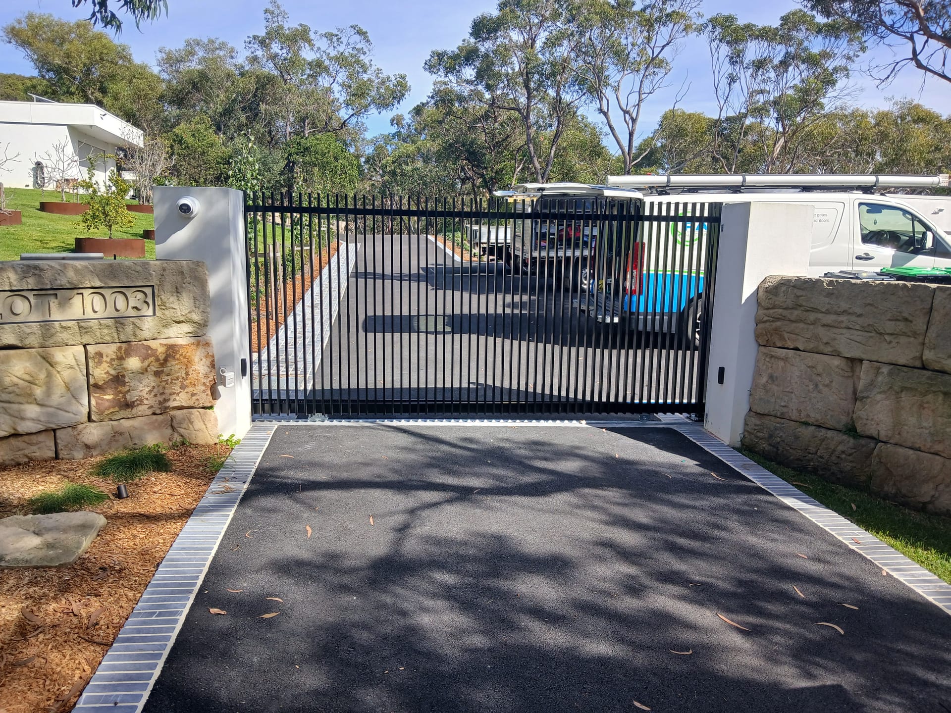 Black automatic sliding gate across a driveway entrance with stone pillars.
