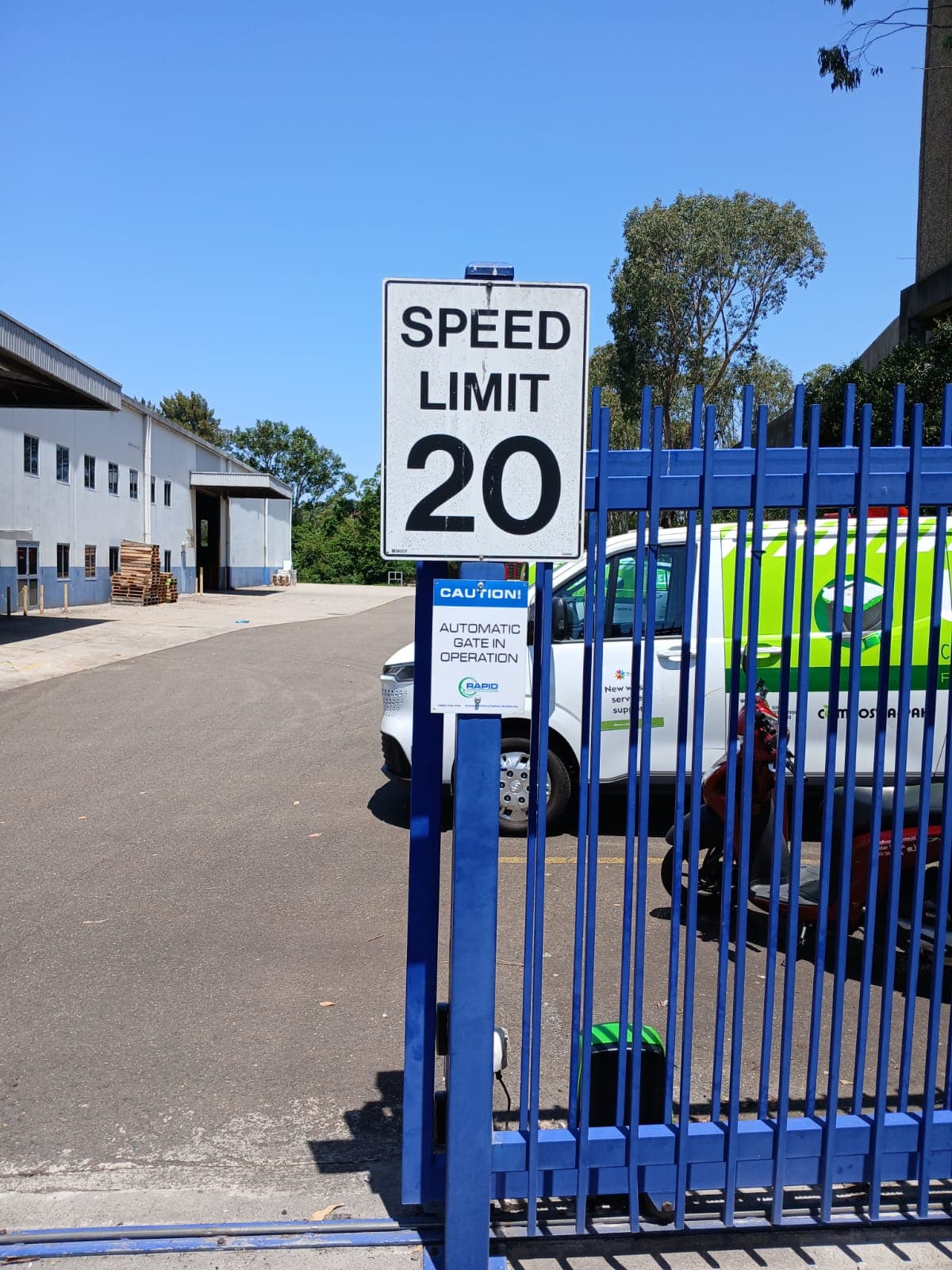 Blue palisade sliding gate with a motor at an industrial vehicle entry.