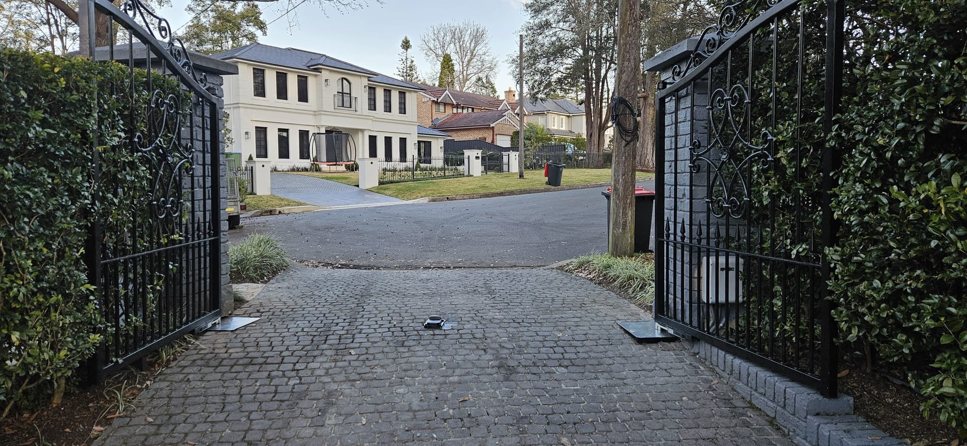 Automatic swing gate openers on black ornamental driveway gates at a residential property entrance.