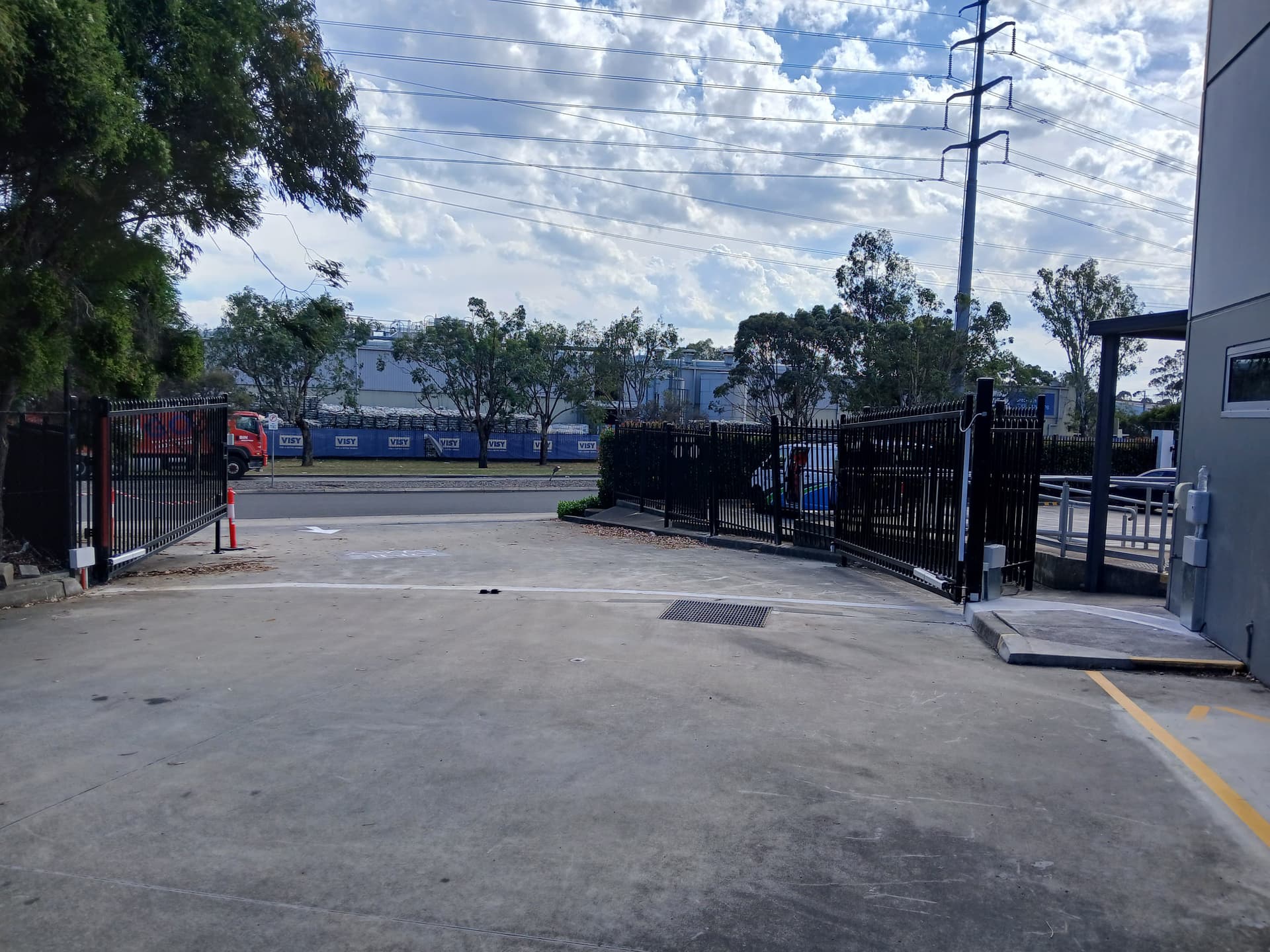 Black vertical bar swing gate at a commercial property driveway access point.