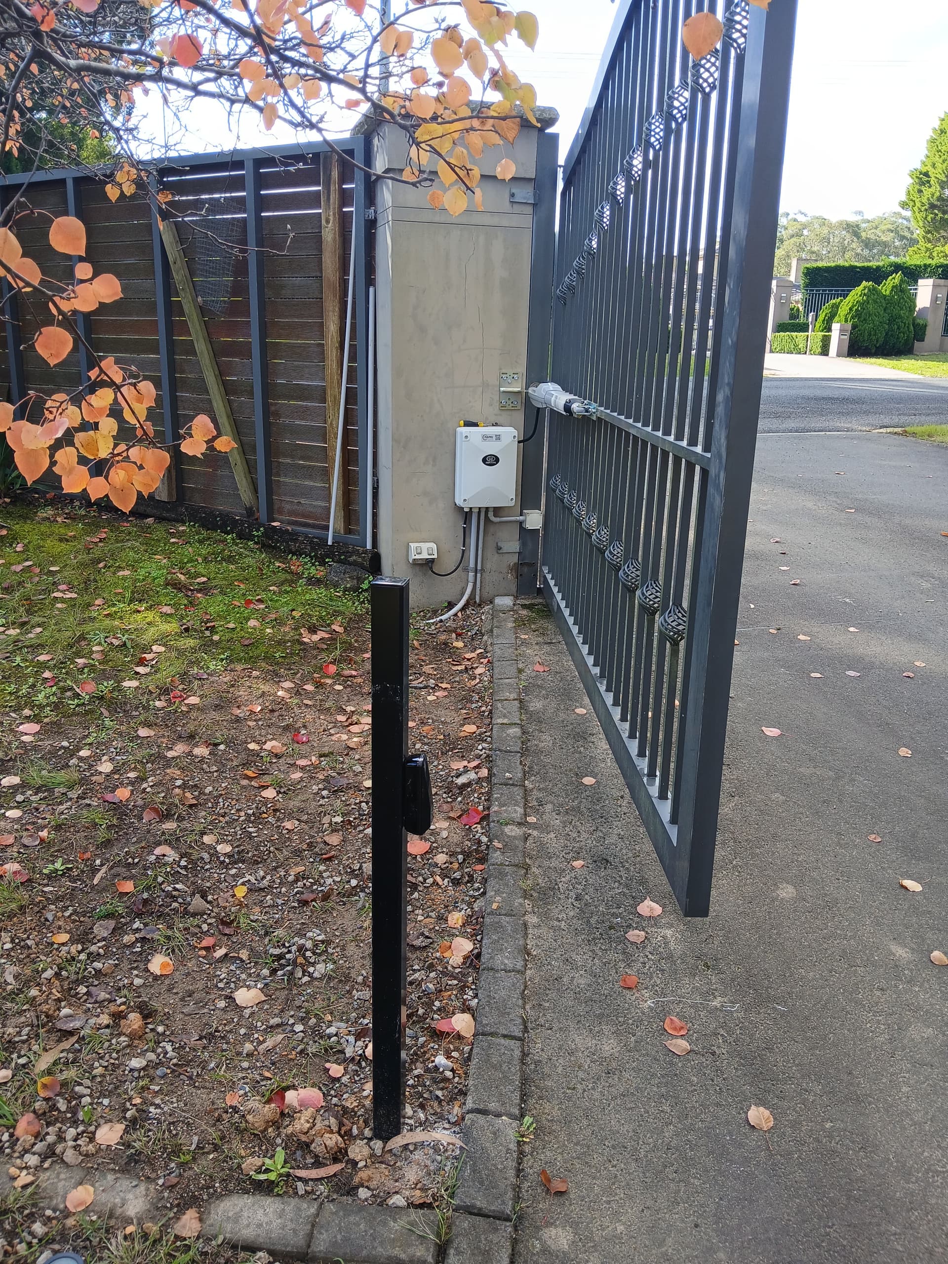 Ornamental residential gate open beside a black gate-side post