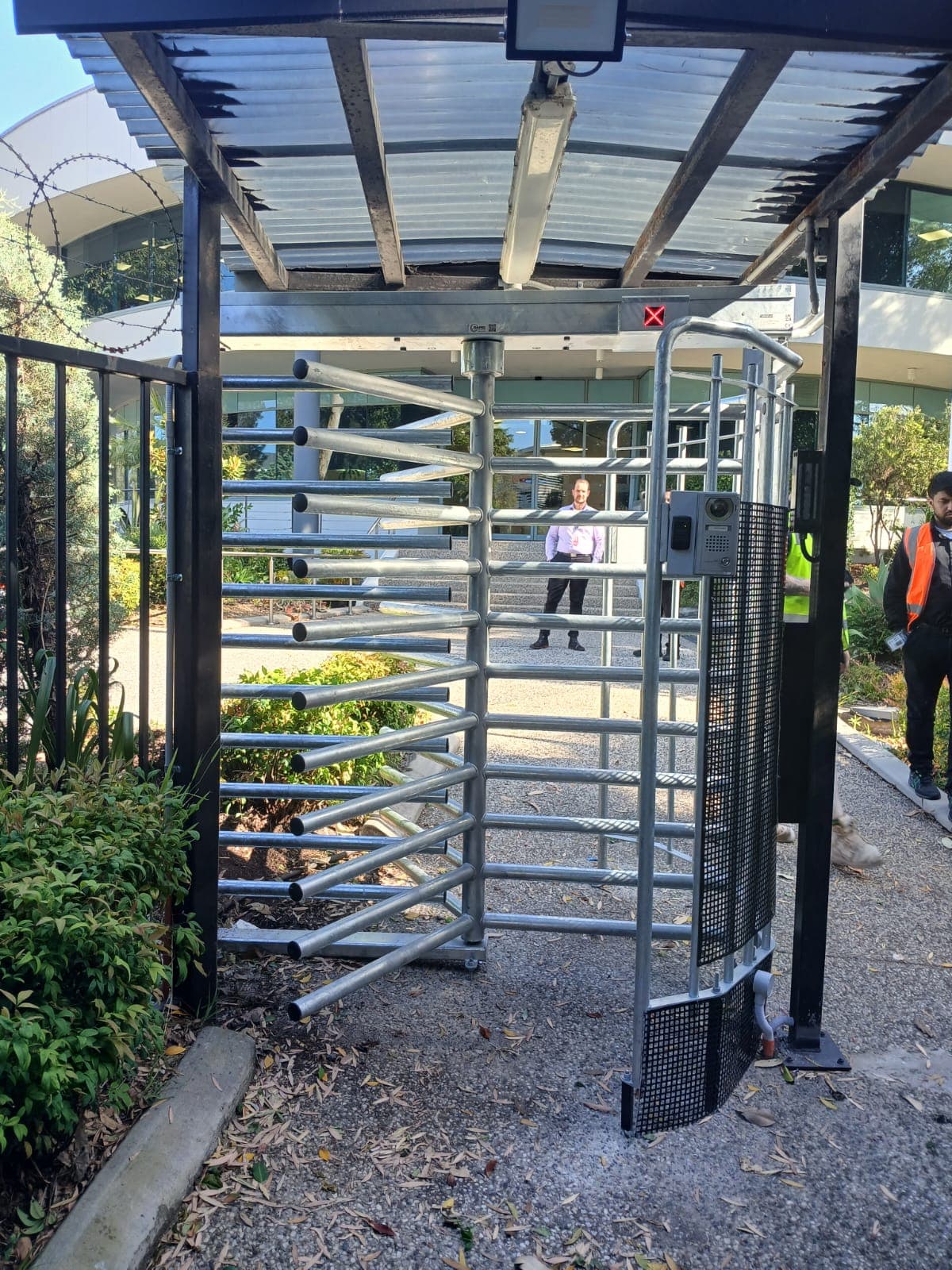 Full-height turnstile installed with a roof, status indicator, mesh side panel and adjacent gate
