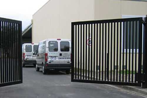 A black double swing gate leading to the car park of a commercial building.