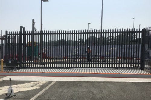 A black track-sliding gate at a train yard.