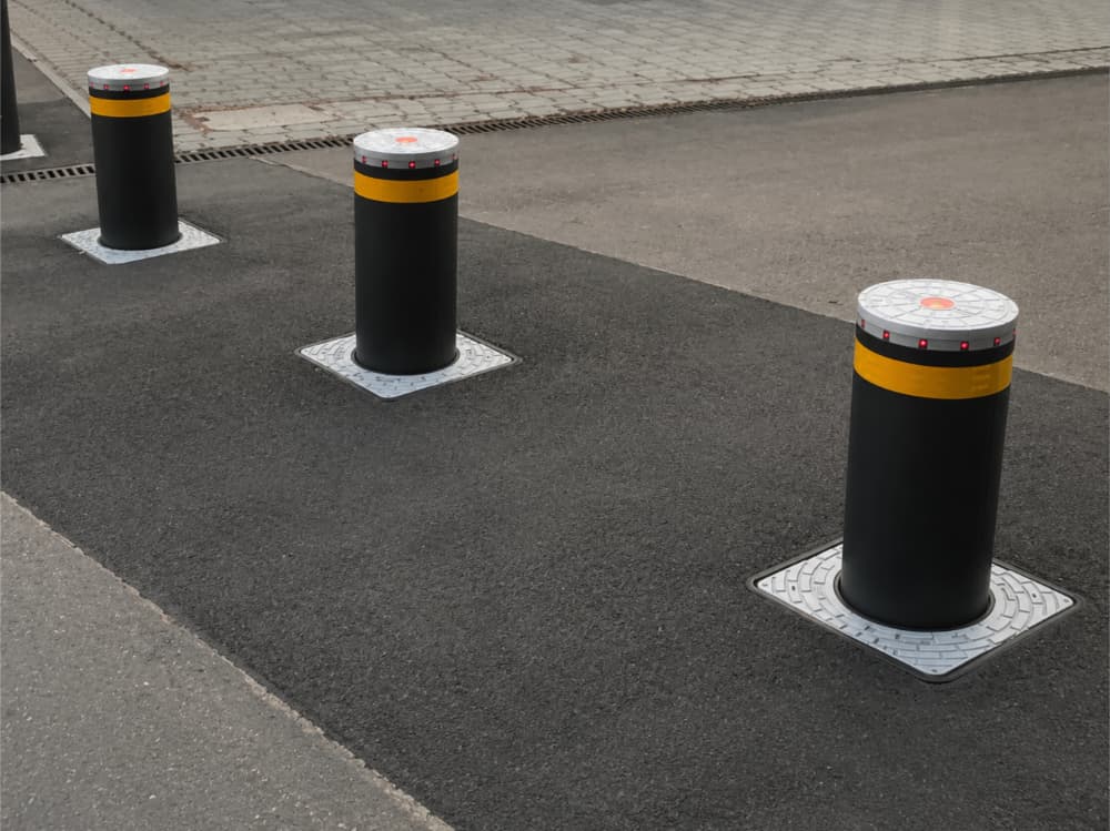 Automatic retractable security bollards raised in a paved roadway access area.